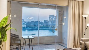 A modern room with a glass door leading to a balcony, a view of a cityscape, a chair, a small table, and a lamp. -  Prime Residence Arkadia (Cairo)