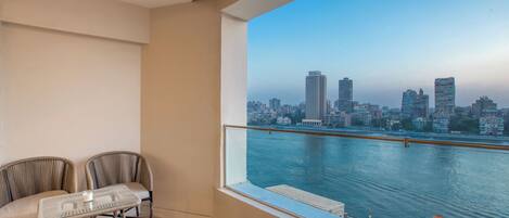 Uma varanda com vista para a cidade, duas cadeiras, uma mesa pequena e um corrimão.