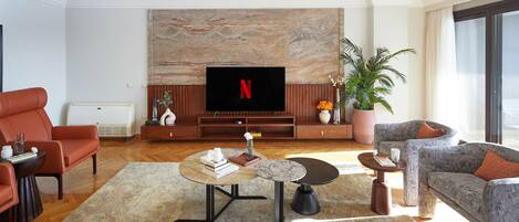 A modern living room with a flat-screen TV, red leather sofa, grey armchair, and a coffee table with books and a vase.