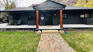 A two-story building with a dark exterior, a covered porch with wooden posts, and a brick pathway leading to the entrance. - Relax and Unwind. Location! Location! Location!Family-friendly. Outdoor space. (Ouray)
