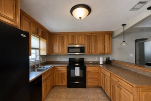 A kitchen with wooden cabinets, a black refrigerator, a stainless steel microwave, and a black stove.