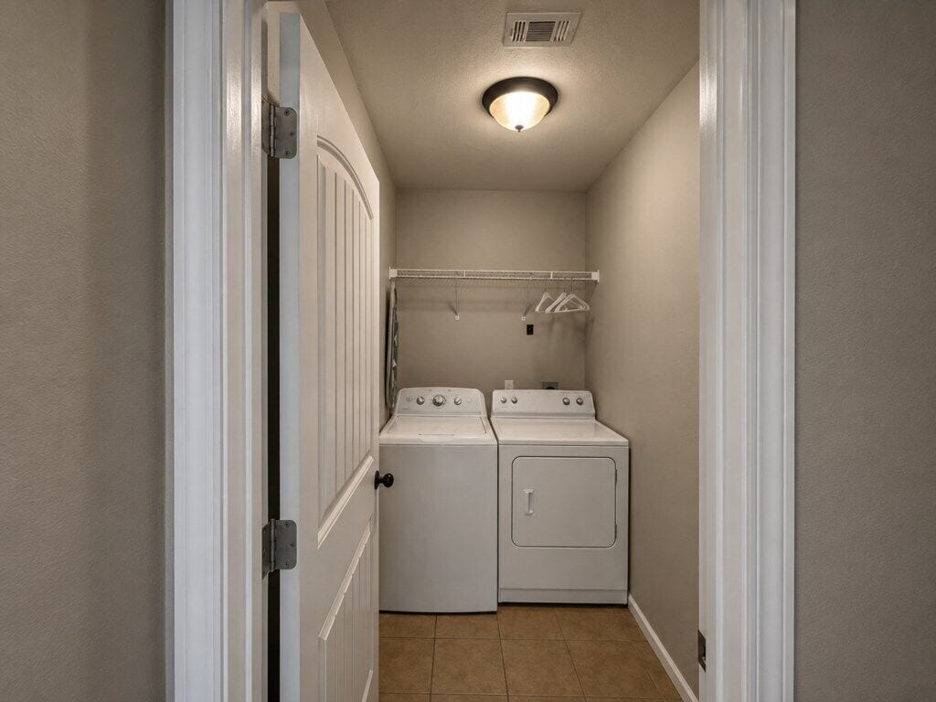A laundry room with two stacked washers and dryers, a clothes drying rack, and a door leading to another room.