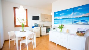 A modern kitchen with white cabinets, a built-in oven, and a microwave. There is a dining area with a white table and chairs, and a window with a view of the sea. - LE VELE BETH'S HOUSE (Brenzone sul Garda)