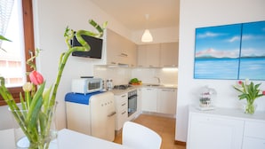A modern kitchen with white cabinets, a microwave, a stove, and a sink. There is a dining table with chairs and a vase with flowers. - LE VELE BETH'S HOUSE (Brenzone sul Garda)