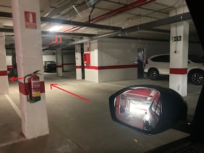 A parking garage with white pillars, red stripes, and a fire extinguisher mounted on a pillar. - Chipiona Santuario Regla Playa Bajo A (Chipiona)