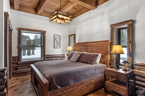 Un dormitorio tipo cabaña de troncos con una cama grande, cabecera de madera y ventana con vistas a árboles.