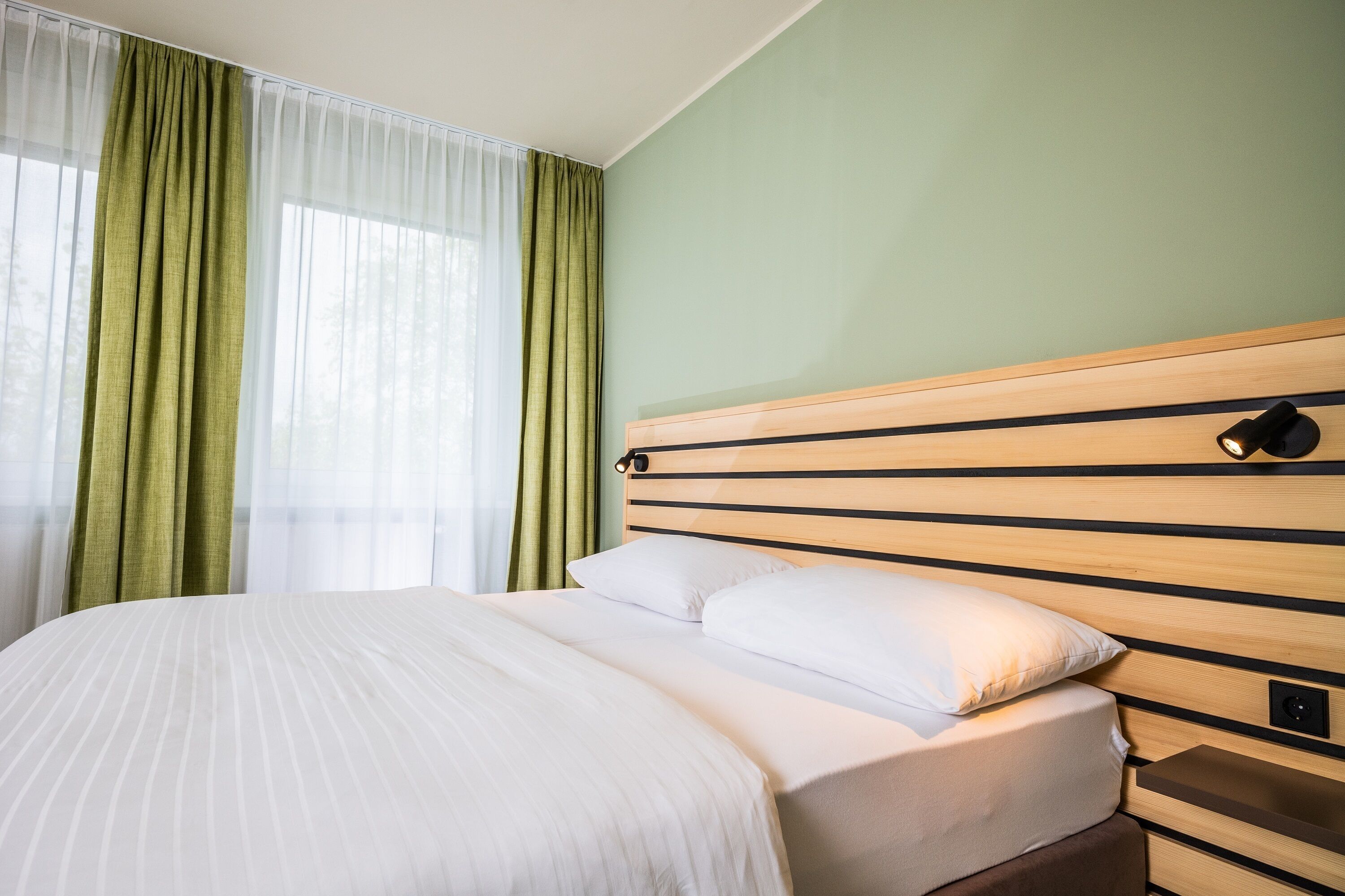 Una habitación de hotel con una cama grande, cabecero de madera y una mesita de noche con lámpara.