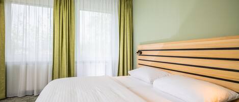 Habitación de hotel con una cama grande, cortinas verdes y un cabecero de madera.