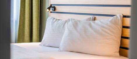 A neatly made bed with white linens and pillows, a wooden headboard, and a green curtain partially drawn to the side.