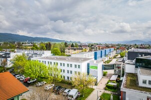 Un hotel moderno con techo plano, zona de estacionamiento y vistas de edificios y colinas circundantes.