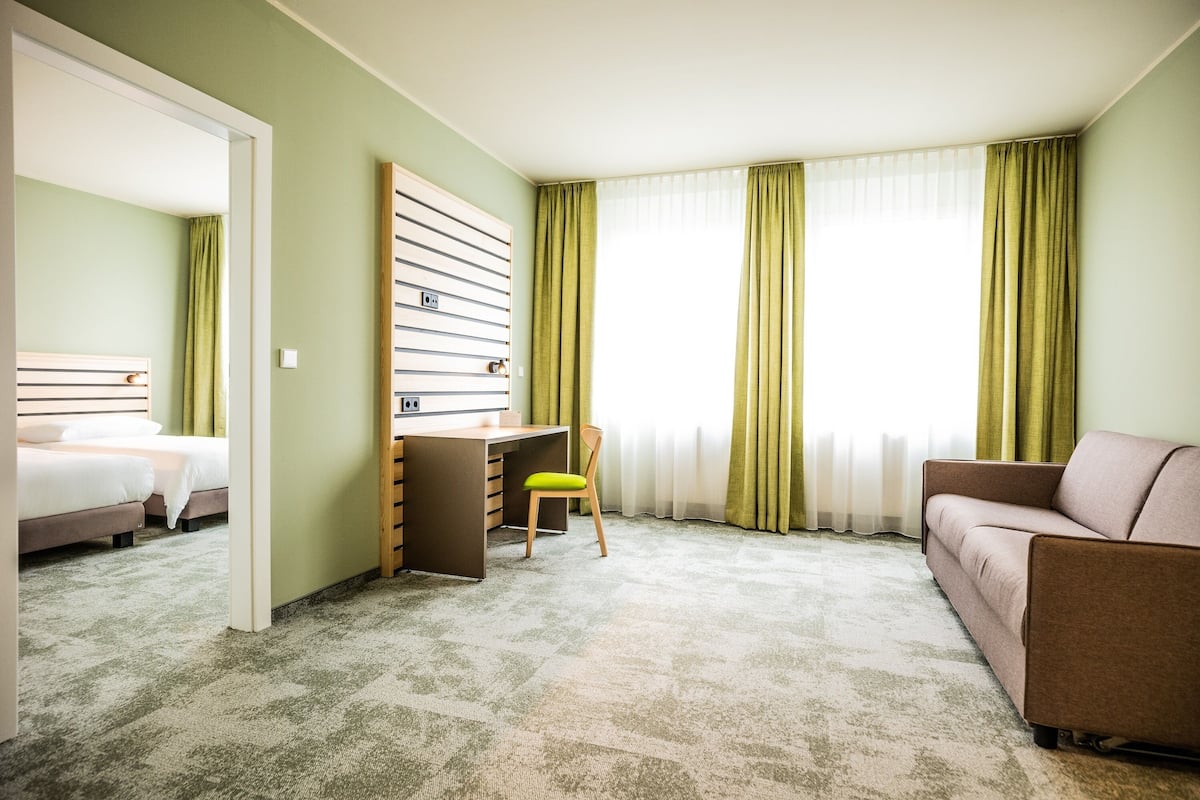 A hotel room with a bed, a desk, a chair, and a sofa.