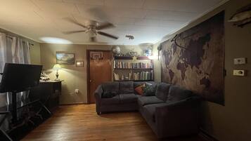 A living room with a grey sectional sofa, a ceiling fan, a bookshelf, and a world map mural on the wall.