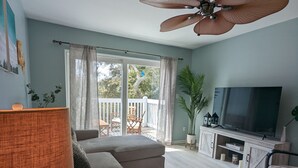 Ein Wohnzimmer mit Sofa, Fernseher, Deckenventilator und Blick ins Freie.