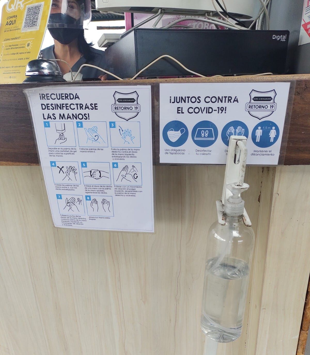 A hand sanitizer dispenser and handwashing instructions at a hotel reception area.
