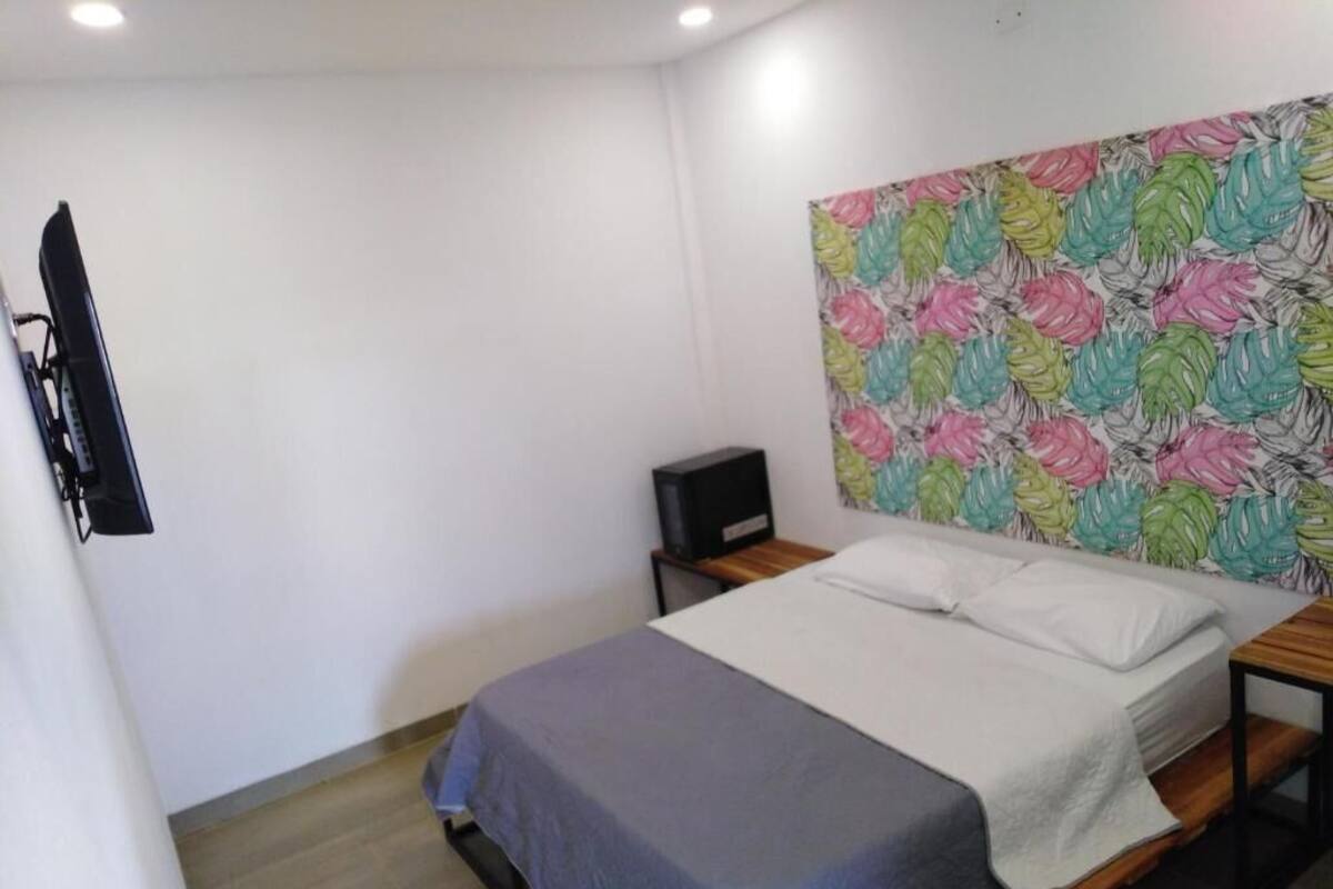 Un dormitorio con cama, televisor montado en la pared y cabecera decorada con motivos de hojas.