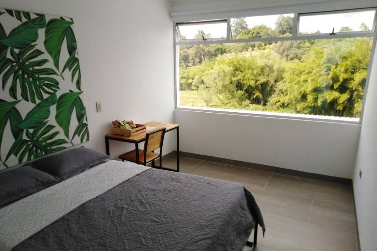 Un dormitorio con una cama, una mesita y un ventanal con vistas a zonas verdes.