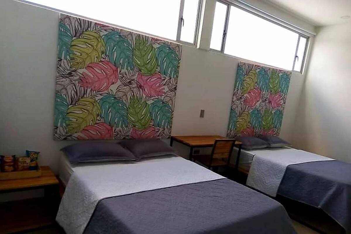 Una habitación con dos camas, una mesa de madera y un ventanal.