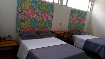 Una habitación con dos camas, una mesa de madera y un ventanal.