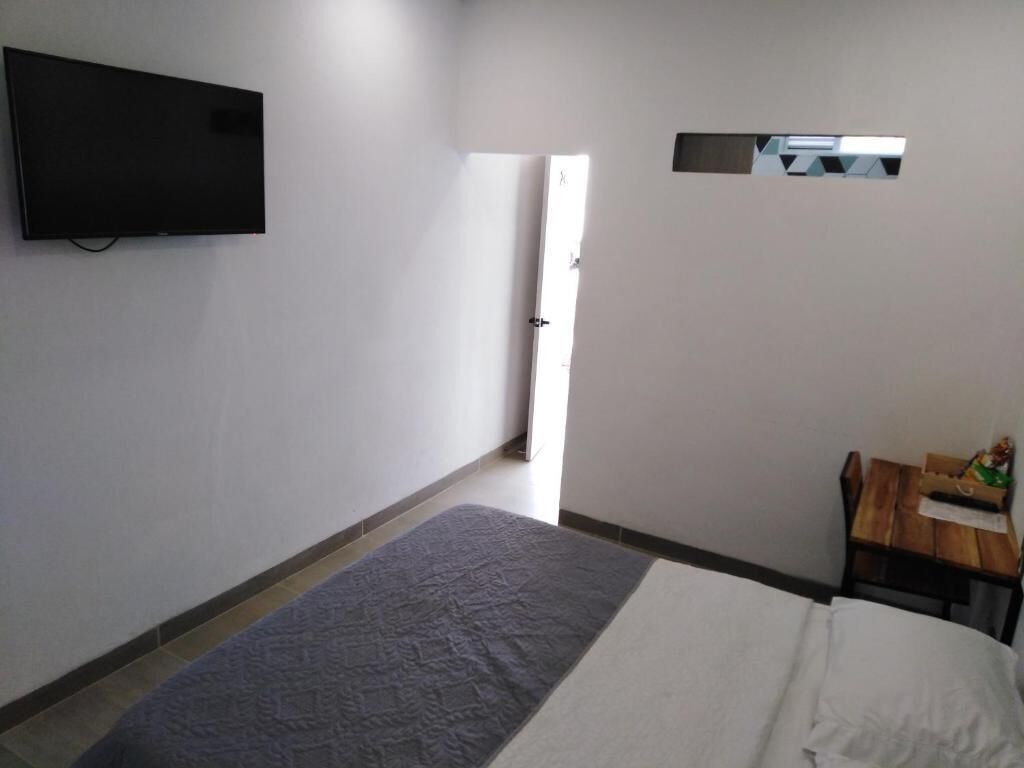 Een hotelkamer met een bed, een aan de muur bevestigde televisie, een klein tafeltje met een stoel en een deur naar een andere kamer.