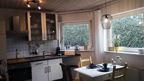 A kitchen with white cabinets, a stove, a sink, and a window with a view of trees. - Apartment "Blume" Vacation made for me (Fahrenbach)