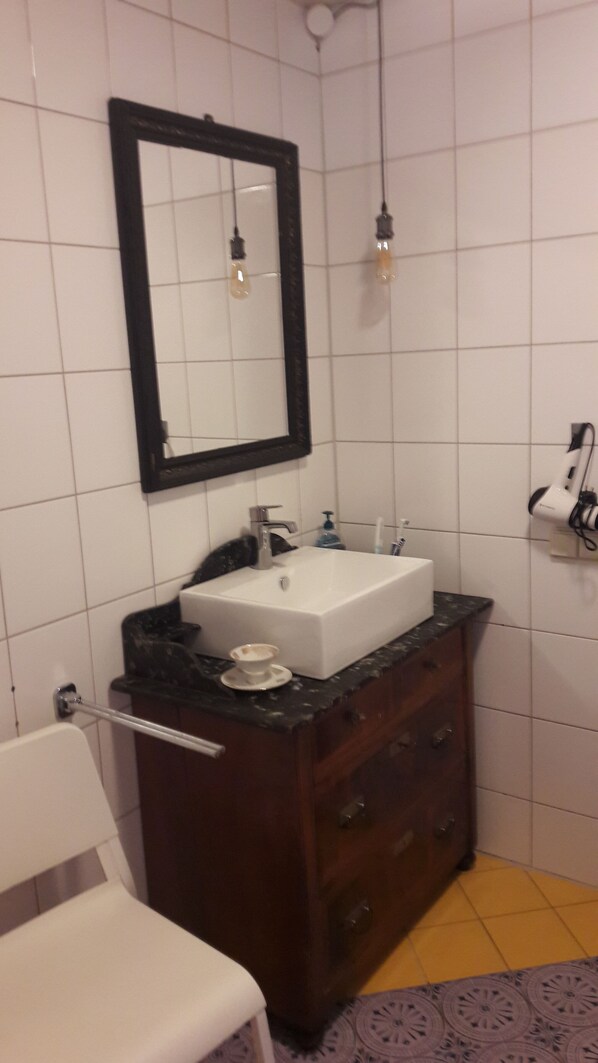 Et badeværelse med en hvid vask, mørkt trækommode, et spejl og en håndklædestang.