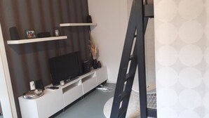 A modern living room with a flat-screen TV, white storage unit, decorative items, and a black ladder. - Apartment "Blume" Vacation made for me (Fahrenbach)