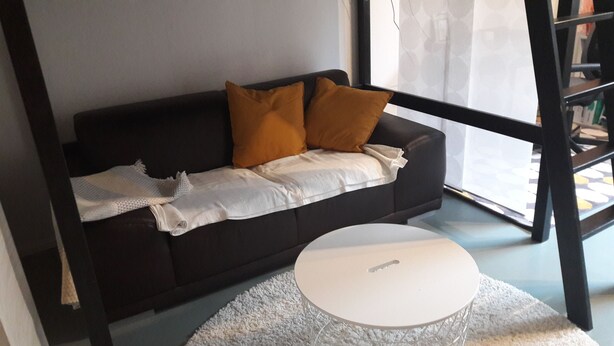 A dark-colored sofa with two pillows, a white throw blanket, and a white round table in front of it. - Apartment "Blume" Vacation made for me (Fahrenbach)