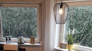 A dining area with a table set for two, chairs, a kettle, and a potted plant by the window. - Apartment "Blume" Vacation made for me (Fahrenbach)
