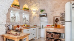 A rustic kitchen with stone walls, wooden cabinets, and a white refrigerator. - Charming Trullo with Heated pool and panoramic view (Cisternino)