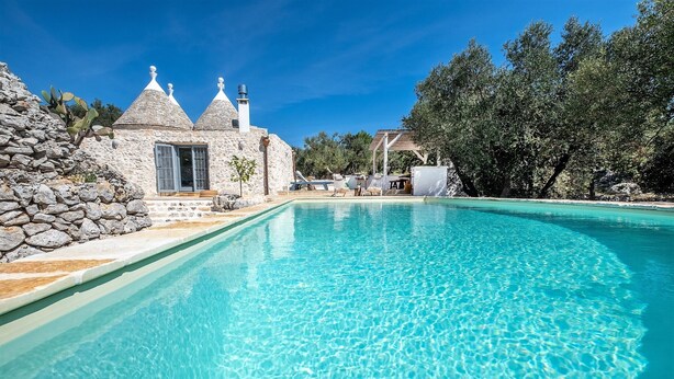 A clear blue pool with stone buildings and a wooden pergola in the background. - Charming Trullo with Heated pool and panoramic view (Cisternino)