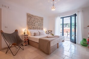 Un dormitorio con cama, una silla, un muro decorativo y vistas a través de un ventanal.