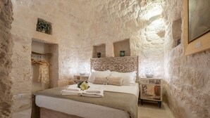 A stone-walled bedroom with a bed, a nightstand, and a shelf with decorative items. - Charming Trullo with Heated pool and panoramic view (Cisternino)
