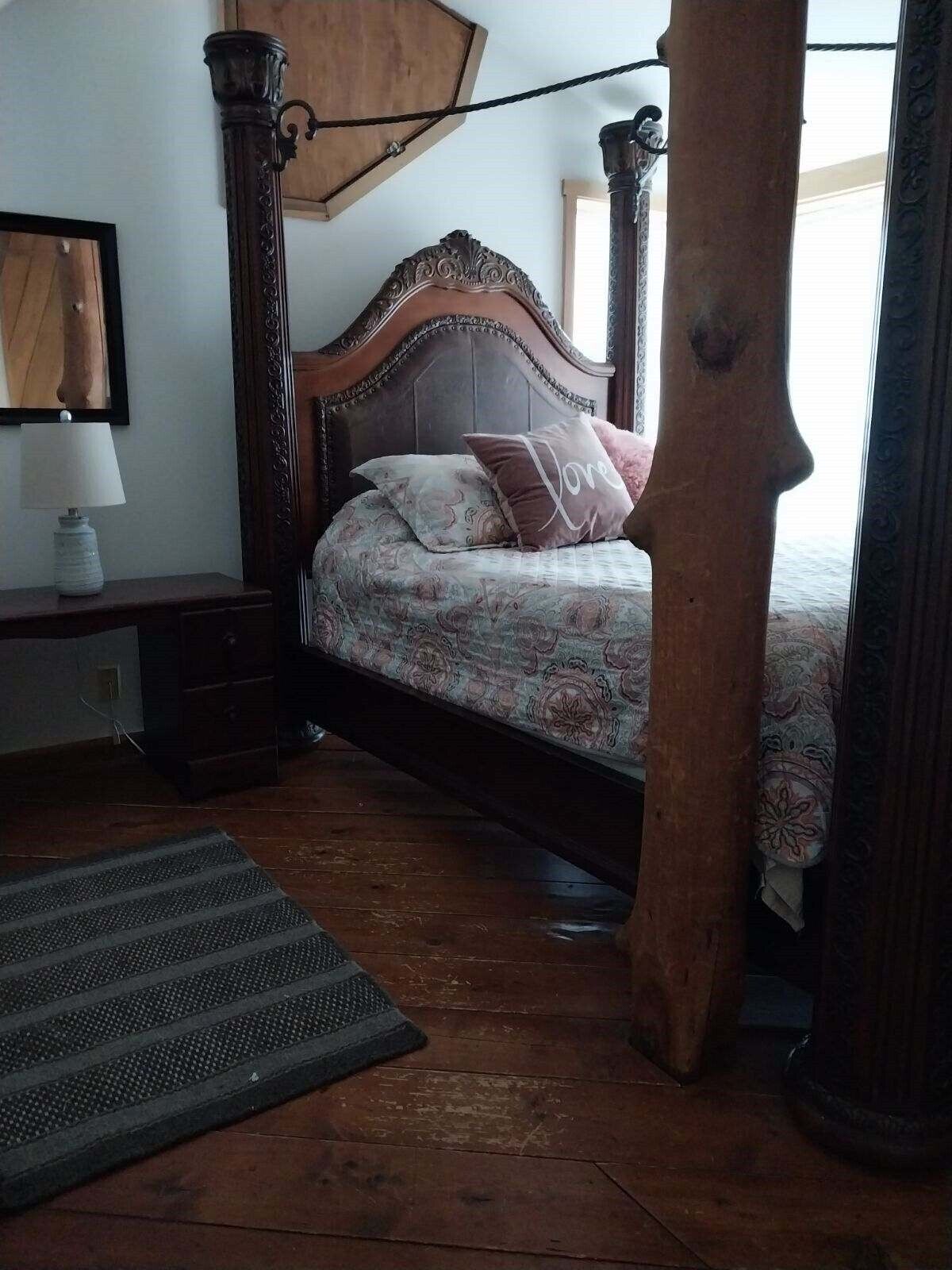 A four-poster bed with a floral bedspread and a pillow with the word "Love".