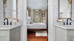 Un baño moderno con lavamanos dobles, un espejo grande y una cama al fondo.