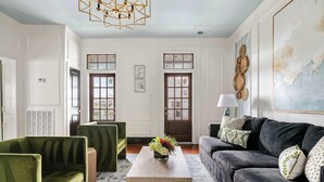 Una sala de estar con un sillón verde, un sofá negro, una mesa de centro de madera y un elemento decorativo en la pared.