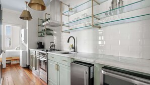 Una cocina moderna con encimera de mármol, electrodomésticos de acero inoxidable y una estantería de vidrio sobre el fregadero.