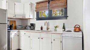 A kitchen with white cabinets, a stove, a sink, a toaster, and a window with blinds. - Stylish Monthly 1BR Downtown Rental (Charleston)