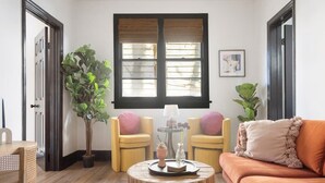 A cozy living room with a round wooden coffee table, two yellow armchairs, a brown sofa, and a large window with blinds. - Stylish Monthly 1BR Downtown Rental (Charleston)