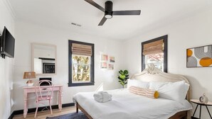 Un dormitorio con cama, escritorio, silla, ventilador de techo y una pequeña mesa con un reloj.