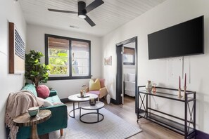 A modern living room with a teal sofa, a round coffee table, and a black TV on the wall.