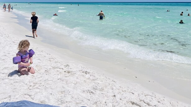 A beach with clear turquoise water, people swimming and walking along the shore. - Steps to the Beach! Water-Taxi to Destin Harbor! 5 Star Property! (Destin)