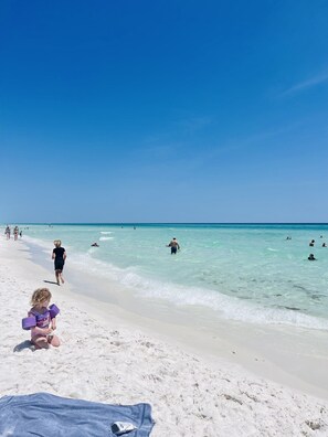 Ein Strand mit klarem türkisblauem Wasser, Menschen beim Schwimmen und Spazierengehen am Ufer.