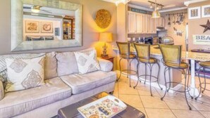 A living room with a sofa, a coffee table, and a dining area with chairs and a table. - Steps to the Beach! Water-Taxi to Destin Harbor! 5 Star Property! (Destin)