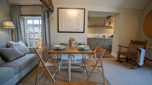 Un salon chaleureux avec une table à manger dressée pour quatre personnes, un canapé et une cuisine en arrière-plan.