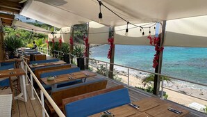 Un espace de restauration en plein air avec des tables en bois et des bancs bleus dotés de coussins, offrant une vue sur la plage.