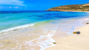 Une plage à l’eau turquoise et limpide, un rivage sablonneux et, au loin, un promontoire rocheux.