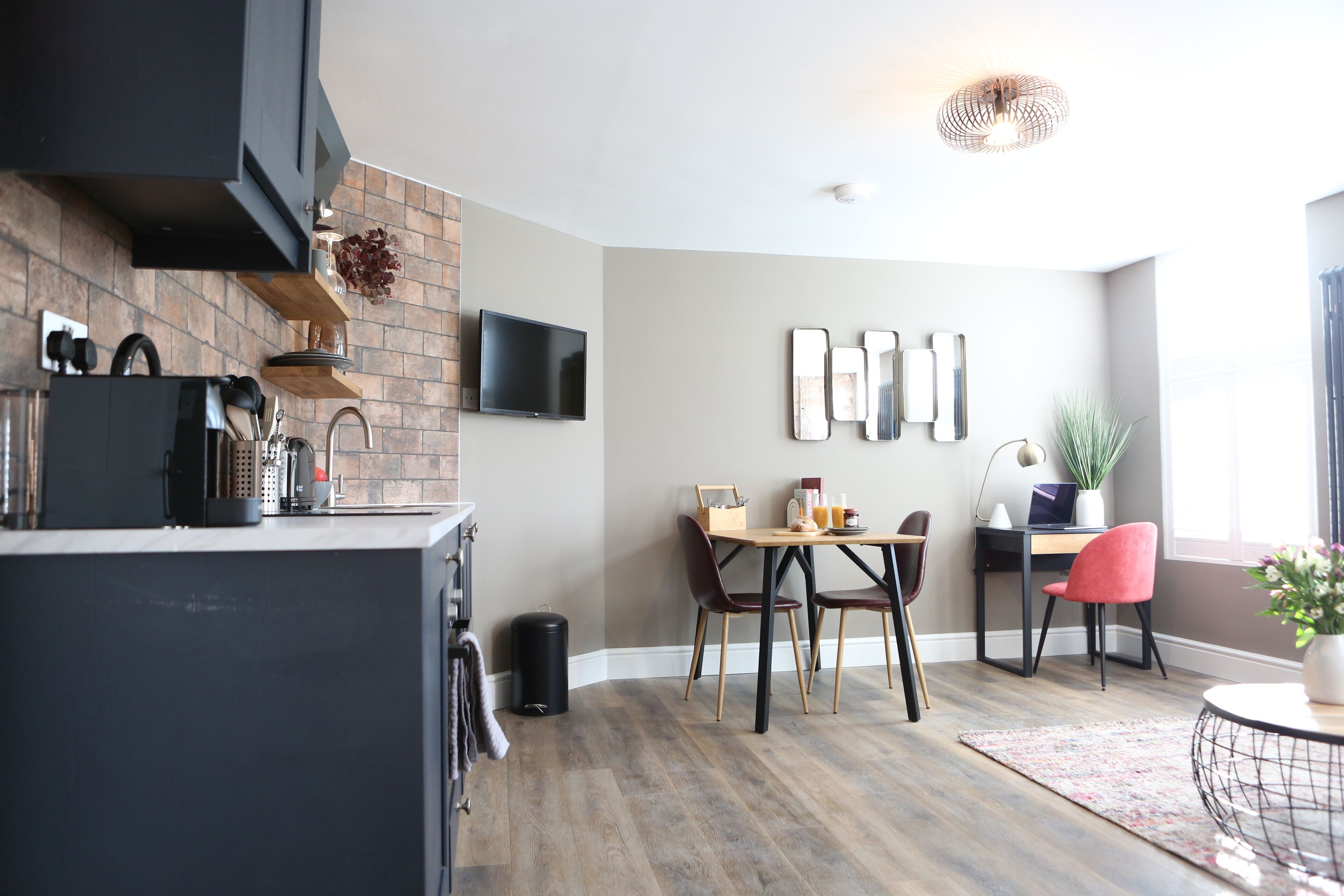 Une cuisine moderne avec un mur de fond en briques, un téléviseur à écran plat et un coin repas comprenant une table et des chaises en bois.