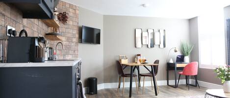 A modern kitchen with a brick backsplash, a flat-screen TV, and a dining area with a wooden table and chairs.