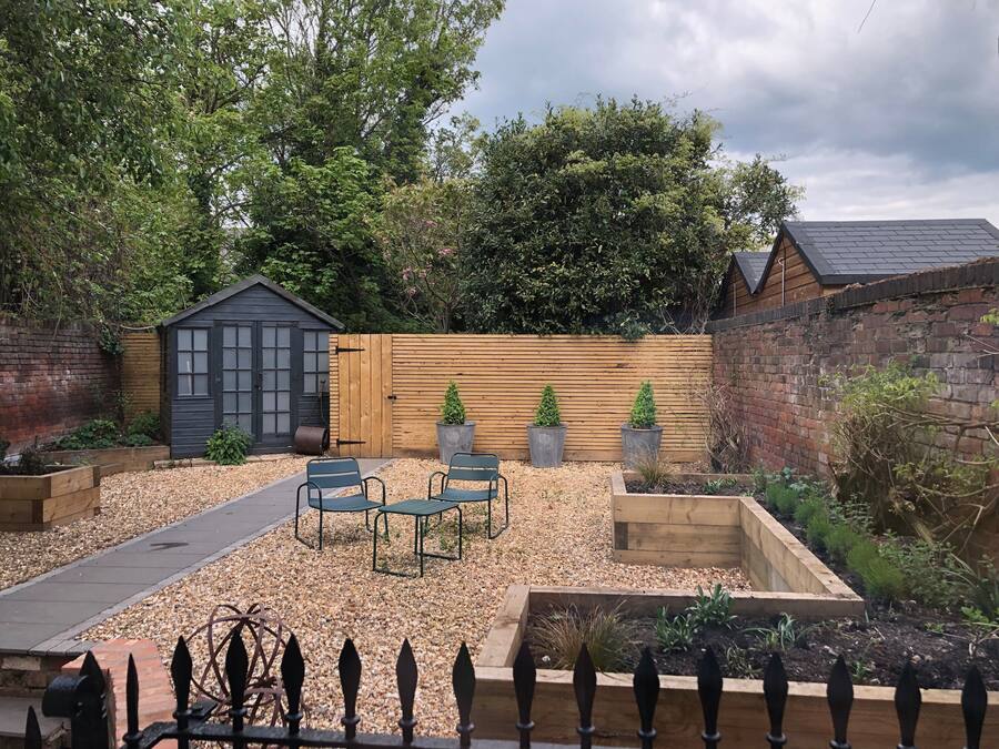 A garden with a wooden fence, a shed, and a seating area with two chairs.