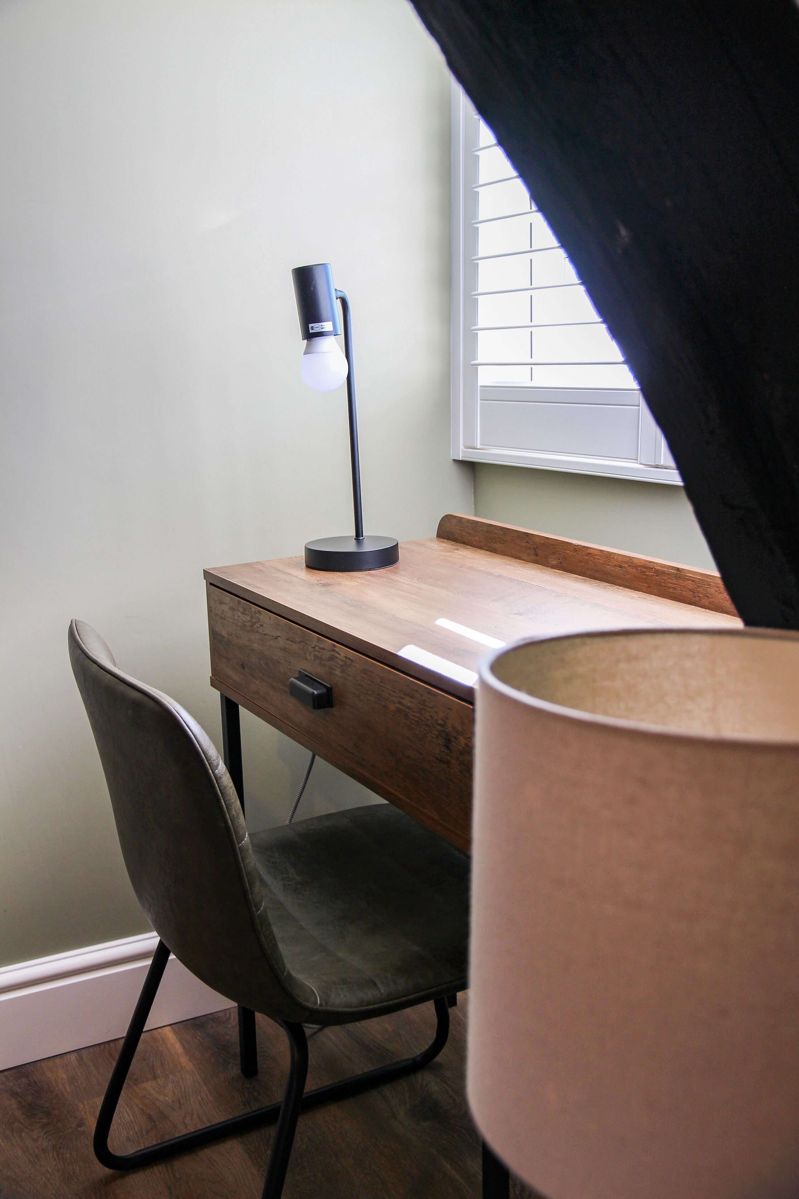 A desk with a lamp, a chair, and a window with blinds.